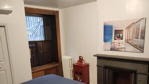 A bedroom with a bed, a fireplace, a window with blinds, and a painting on the wall.
