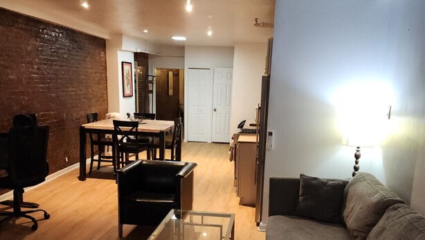 A living room with a sofa, a glass coffee table, a dining area with a table and chairs, and a kitchen area with a refrigerator.