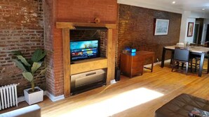 A living room with a fireplace, a television, a dining area, and a potted plant.