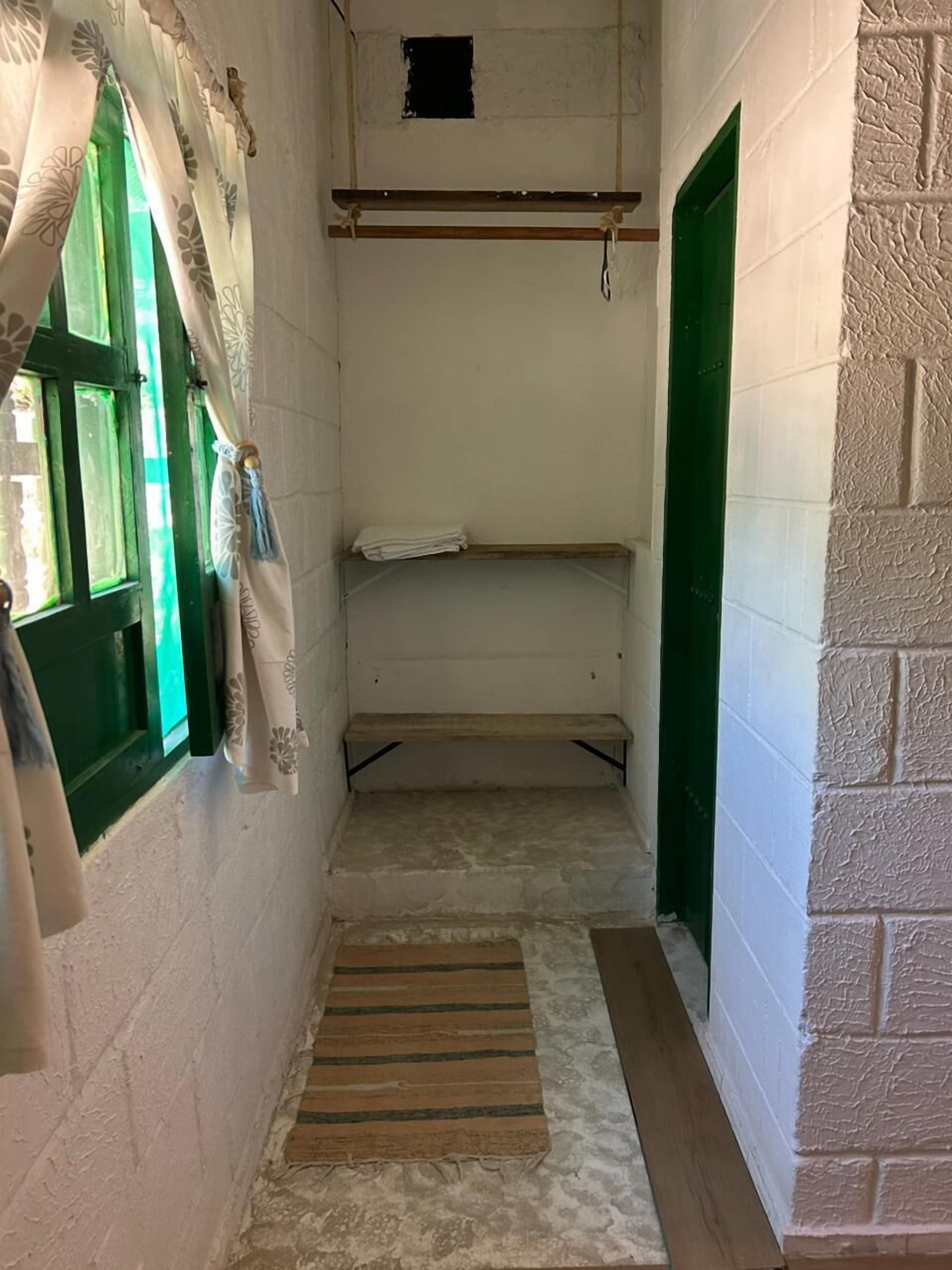 A narrow hallway with a wooden bench, a small window with green shutters, and a door with a green frame.