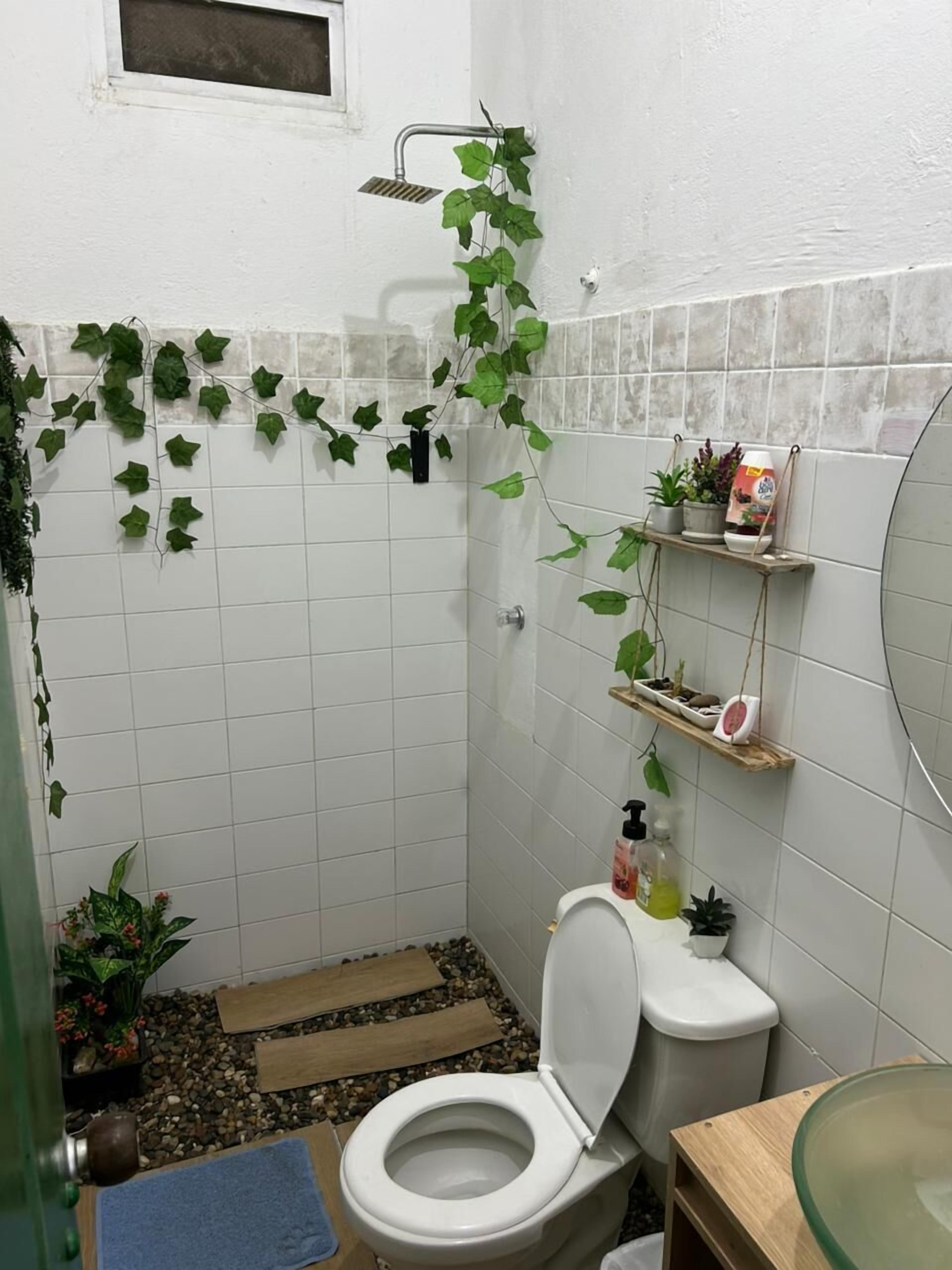 Un baño pequeño con azulejos, ducha, inodoro y un estante con artículos de aseo.