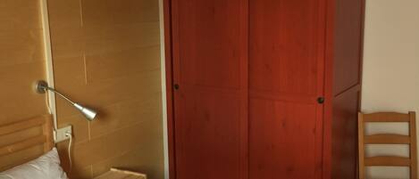 A bedroom with a wooden bed, a red wardrobe, a wooden chair, and a hanging light fixture.