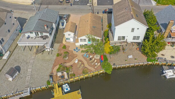 Vista aérea de una propiedad frente al agua con muelle, un barco pequeño y una casa con terraza y zona de estar al aire libre.