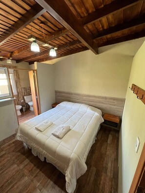 A bedroom with a wooden ceiling, a bed with a white duvet, a bedside table, and a window with curtains. - Olivos de Monte (San Miguel del Monte)