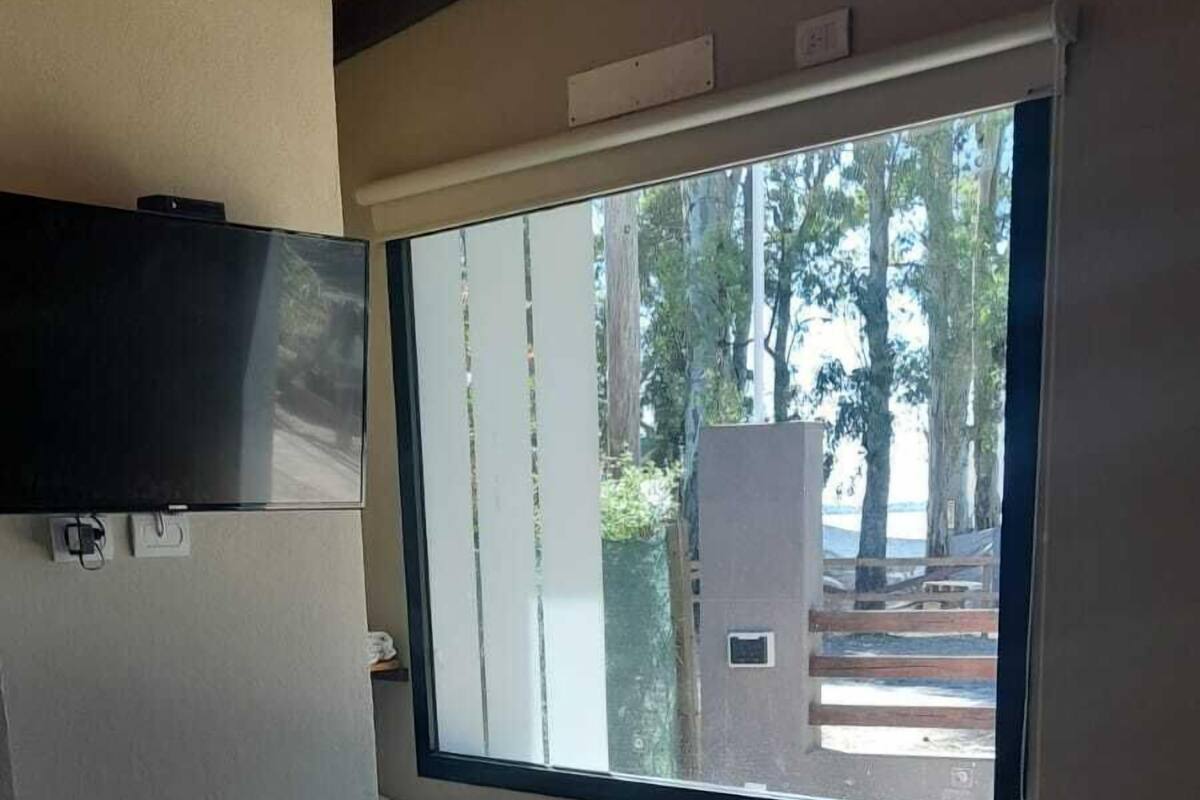 Un dormitorio con un ventanal grande, una cama con colcha y una mesita.