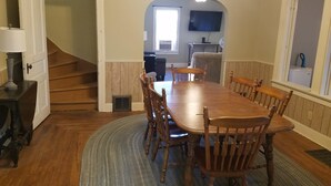 Une salle à manger avec une table et des chaises en bois, un escalier et une vue sur un espace cuisine.