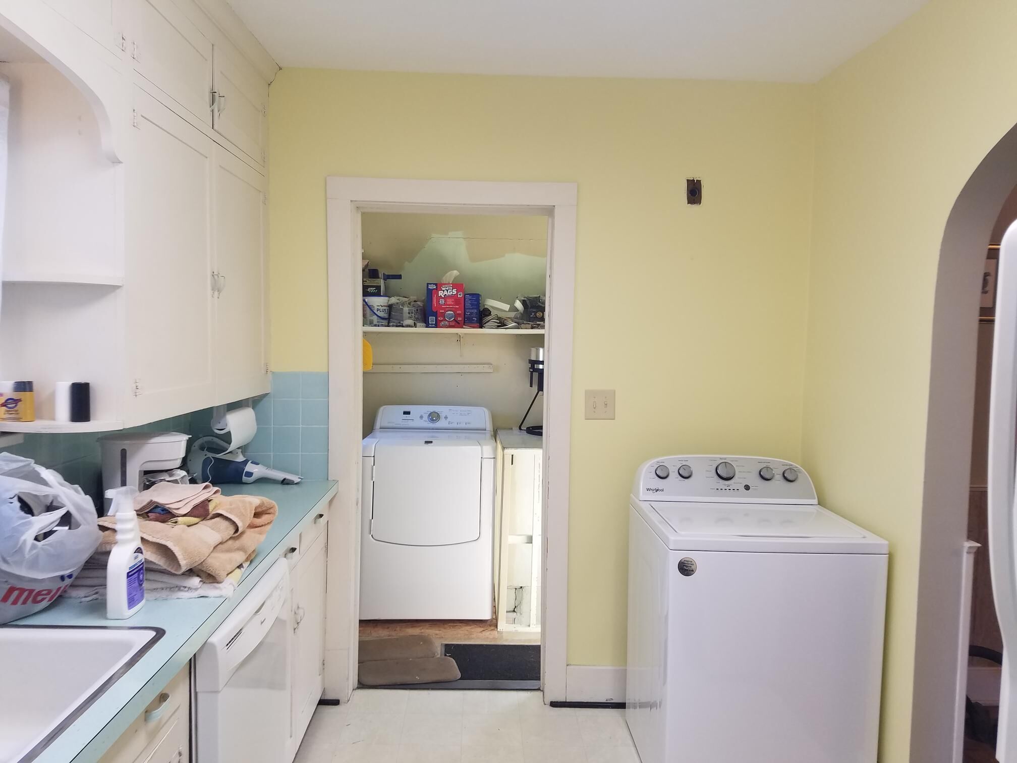 A laundry room with a washer and dryer, a small shelf with cleaning supplies, and a door leading to a storage area.