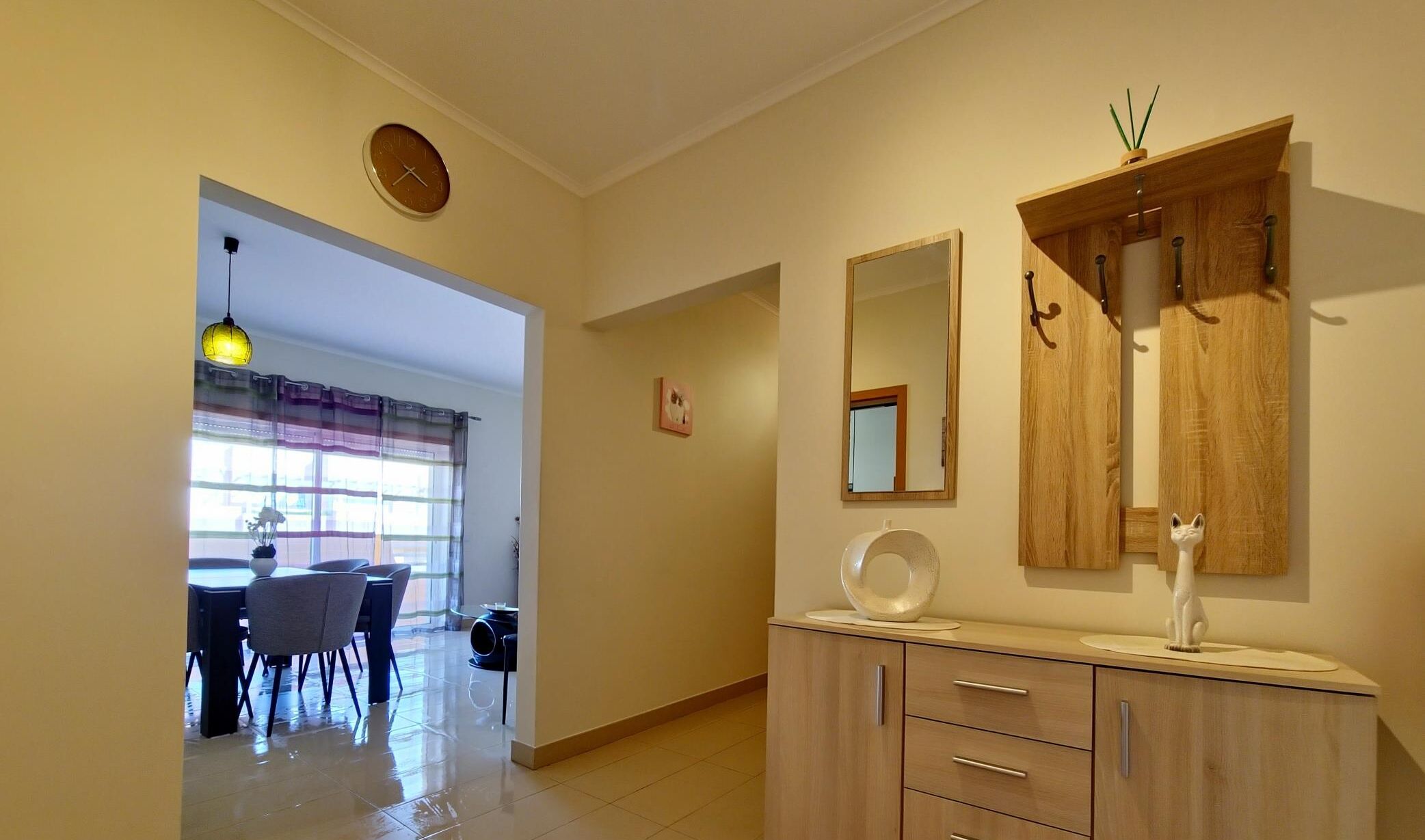 Une pièce avec un meuble en bois, un miroir et une horloge au mur.