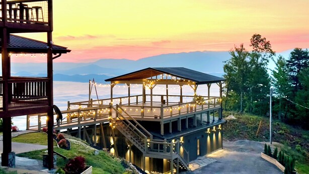 A wooden deck with a gazebo, surrounded by greenery and overlooking a body of water with mountains in the distance. - 360 Views~Indoor Pool~Theater~Game Room~Mini Golf~Fireplaces (Sevierville)