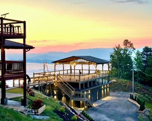 A wooden deck with a gazebo, surrounded by greenery and overlooking a body of water with mountains in the distance. - 360 Views~Indoor Pool~Theater~Game Room~Mini Golf~Fireplaces (Sevierville)
