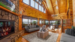 A spacious living area with a stone fireplace, a gray sofa, and a wooden coffee table. - 360 Views~Indoor Pool~Theater~Game Room~Mini Golf~Fireplaces (Sevierville)