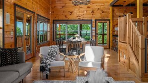 A spacious wooden cabin with a dining area, a sofa, and a fireplace. - 360 Views~Indoor Pool~Theater~Game Room~Mini Golf~Fireplaces (Sevierville)