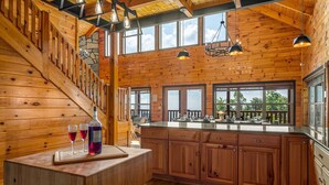 A wooden cabin interior with a kitchen, dining area, and a staircase. - 360 Views~Indoor Pool~Theater~Game Room~Mini Golf~Fireplaces (Sevierville)