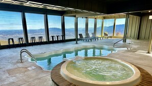 A spa area with a hot tub, lounge chairs, and a view of the mountains through large windows. - 360 Views~Indoor Pool~Theater~Game Room~Mini Golf~Fireplaces (Sevierville)
