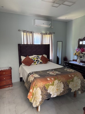A bedroom with a bed, a dresser, a mirror, and an air conditioning unit.