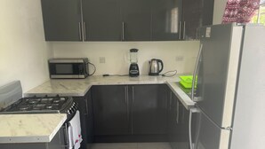 Una cocina compacta equipada con estufa a gas, microondas, licuadora, hervidor y refrigerador.