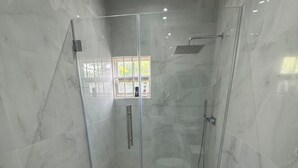 Un baño con ducha acristalada, inodoro y una pequeña ventana.