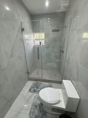 A bathroom with a glass-enclosed shower, a toilet, and a small window.