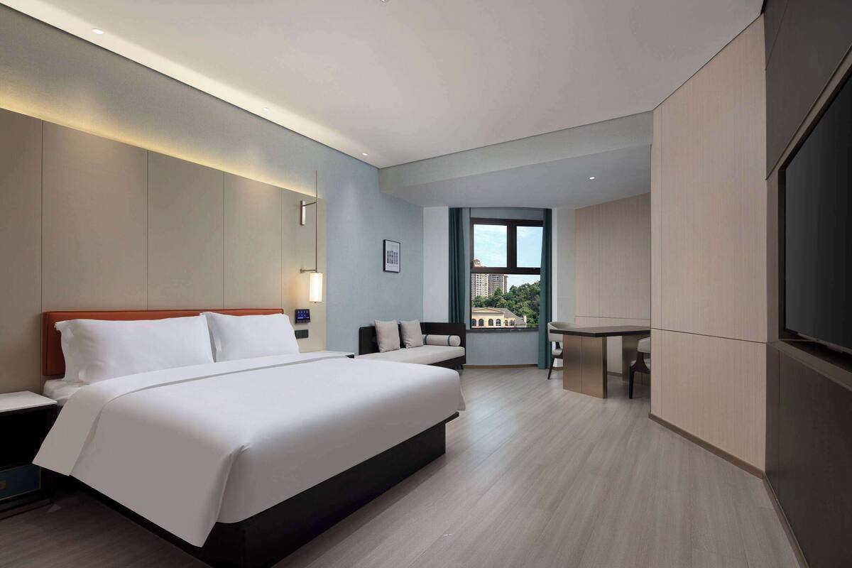 A modern hotel room with a large bed, a desk, and a view of the city.