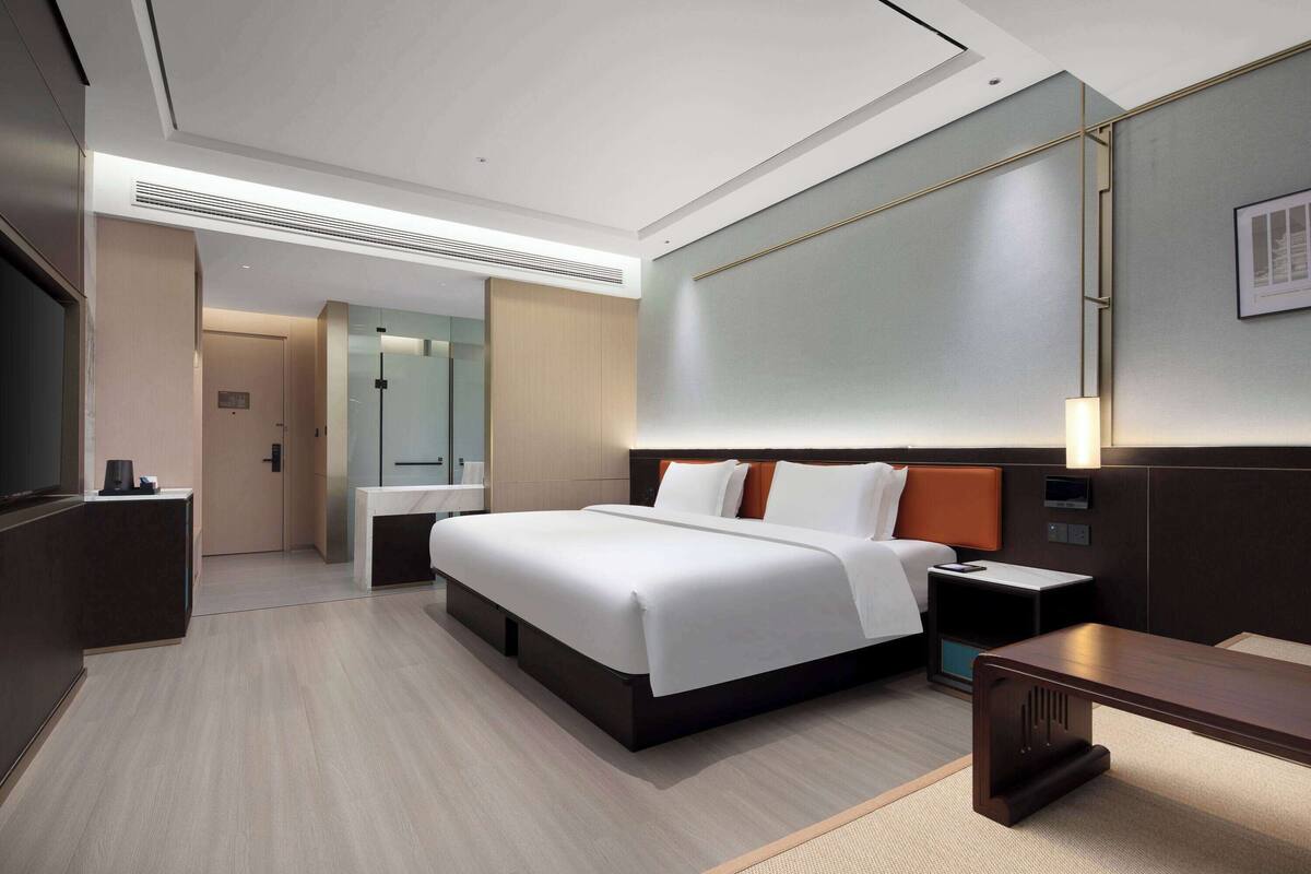 A modern hotel room with a large bed, bedside tables, a desk, and a mirror.