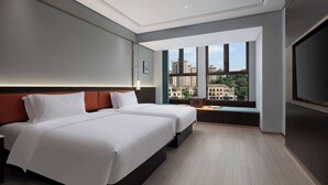 Una habitación de hotel moderna con dos camas, un ventanal grande con vistas a la ciudad y un televisor de pantalla plana.