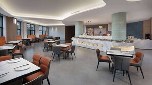 Un comedor moderno con mesas y sillas, una barra central con exhibición, y grandes ventanales que permiten la entrada de luz natural.