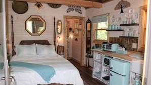 Um quarto aconchegante com uma cama grande, cabeceira de madeira e cozinha retrô com geladeira e fogão.