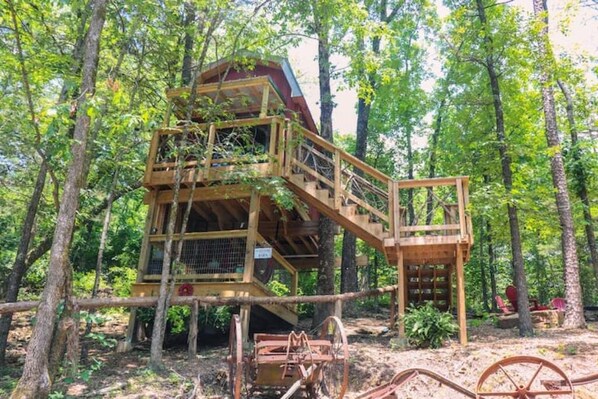 A wooden treehouse with multiple levels and a staircase, surrounded by dense forest. - Greers Ferry Lake Treehouses (Edgemont)