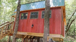 A red wooden treehouse with a metal roof, surrounded by trees.