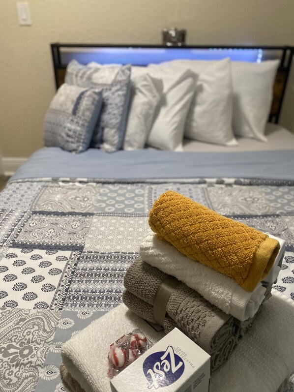 A neatly made bed with a patterned bedspread, a rolled-up towel, and a box of tissues.