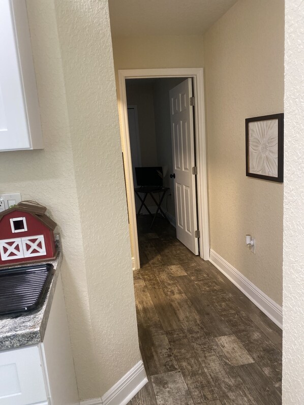 A hallway with a wooden floor, a door leading to another room, and a framed picture on the wall.