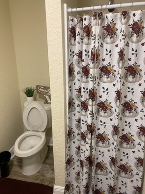 A bathroom with a toilet, a shower curtain with a floral pattern, and a sign that says "Family".