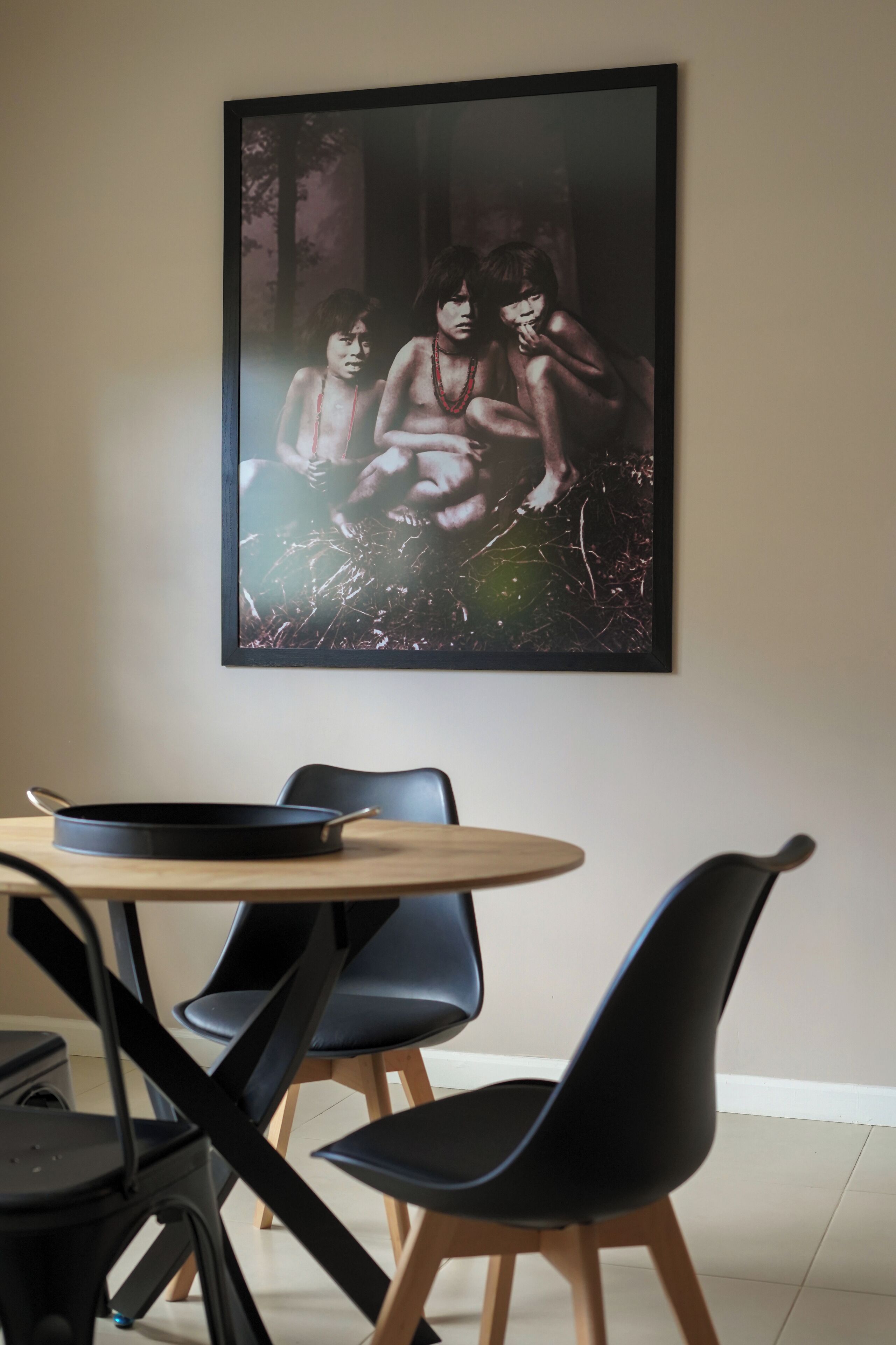 A dining area with a round table, black chairs, and a framed picture on the wall.
