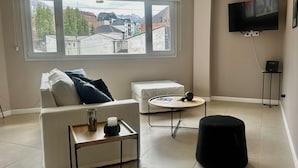 A modern living room with a sofa, a small round table, a black ottoman, and a TV mounted on the wall. - Gente del Sur - Yehuin (Ushuaia)