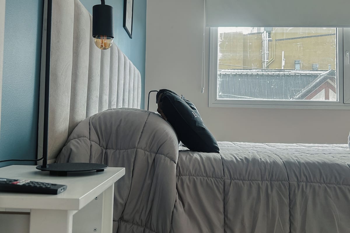 Quarto com cama, escrivaninha, luminária e janela.