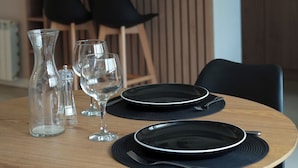 A dining table set with plates, glasses, and a pitcher, with chairs and a kitchen in the background. - Gente del Sur - Yehuin (Ushuaia)