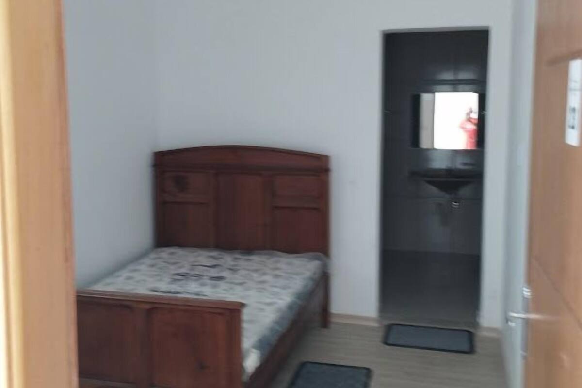 A narrow hallway with a wooden bed, a small bathroom, and a door leading to another room.