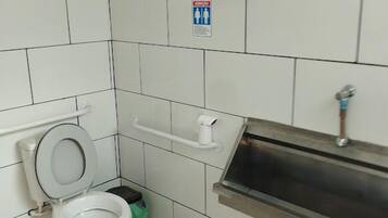 A small, clean bathroom with white tiles, a toilet, a sink, and a trash bin.