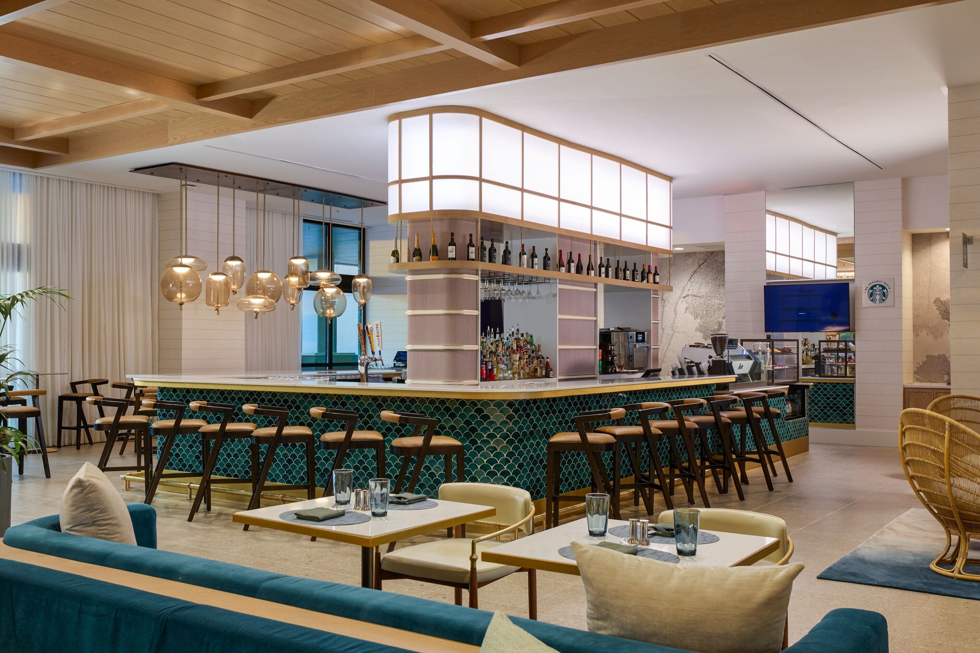 A modern bar area with a curved counter, multiple seating options including bar stools and tables, and a variety of bottles and glasses on shelves.