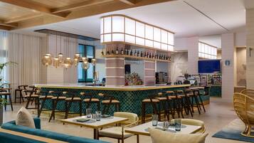 A modern bar area with a curved counter, multiple seating options including bar stools and tables, and a variety of bottles and glasses on shelves.