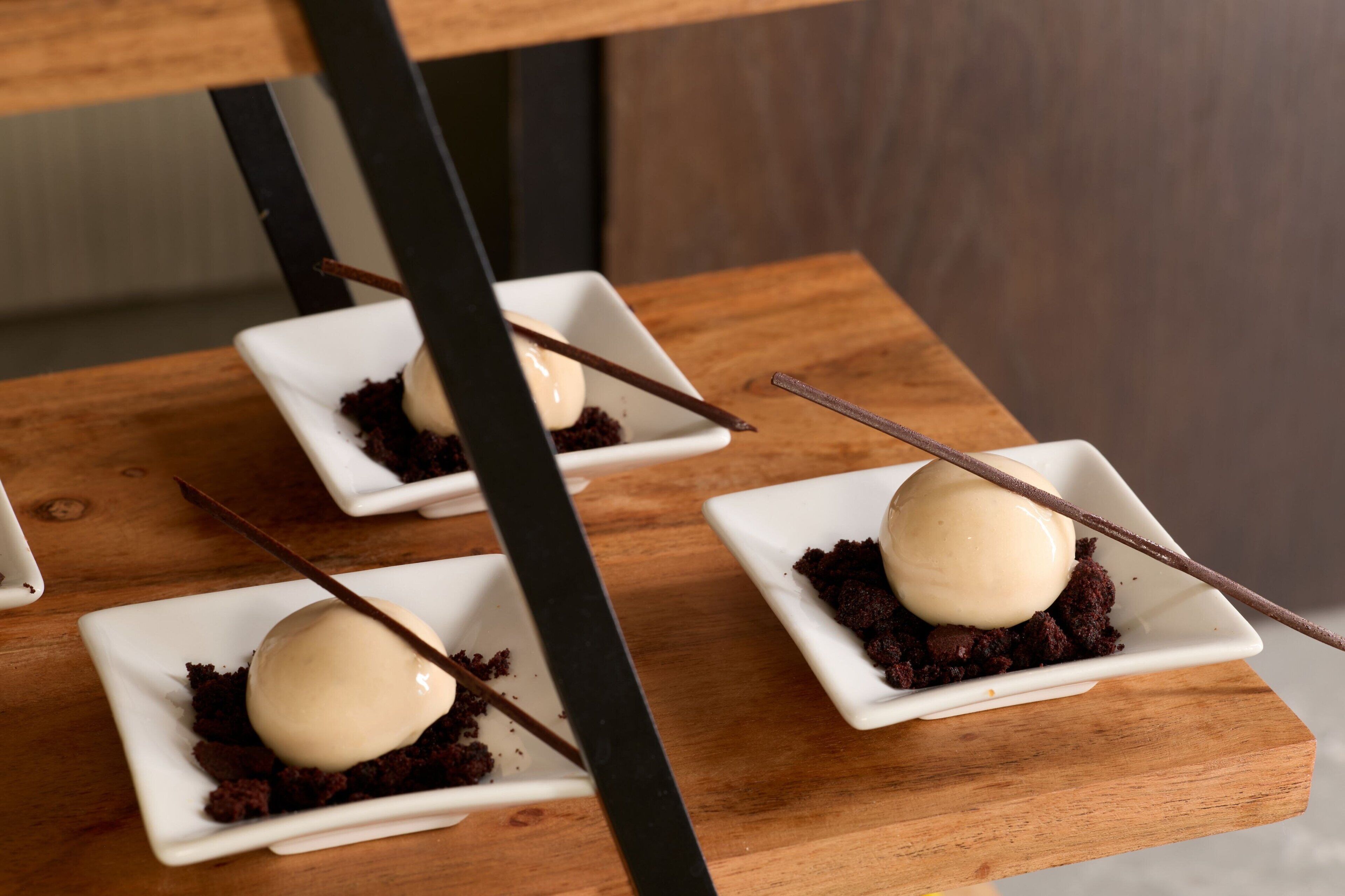 Three square white dishes with chocolate cake and a scoop of vanilla ice cream, each with a chocolate stick.