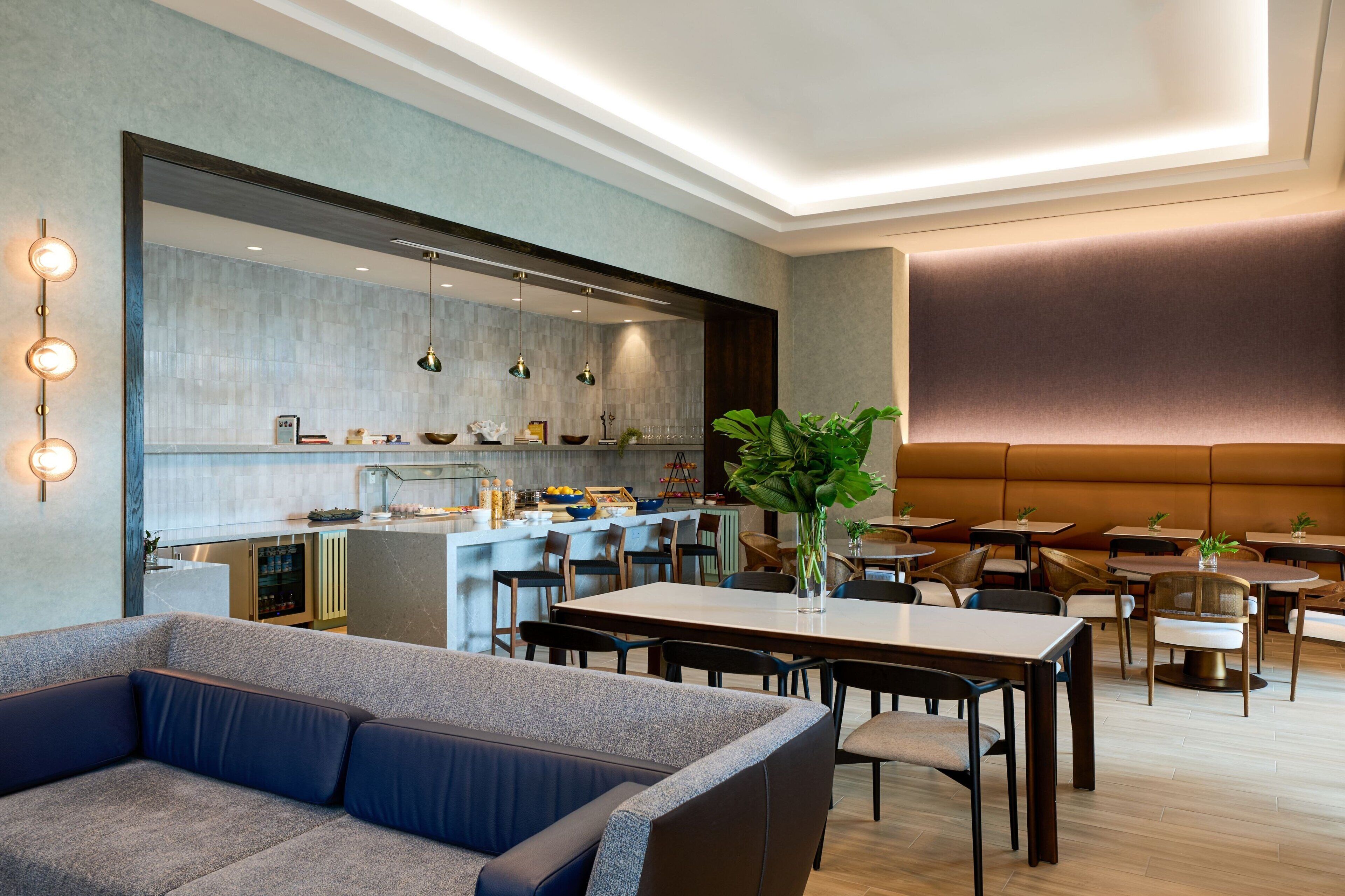 A modern dining area with a sofa, tables, and chairs. A kitchen is visible in the background.