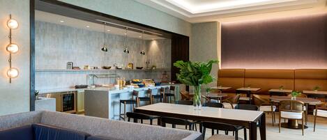 A modern dining area with a sofa, tables, and chairs. A kitchen is visible in the background.