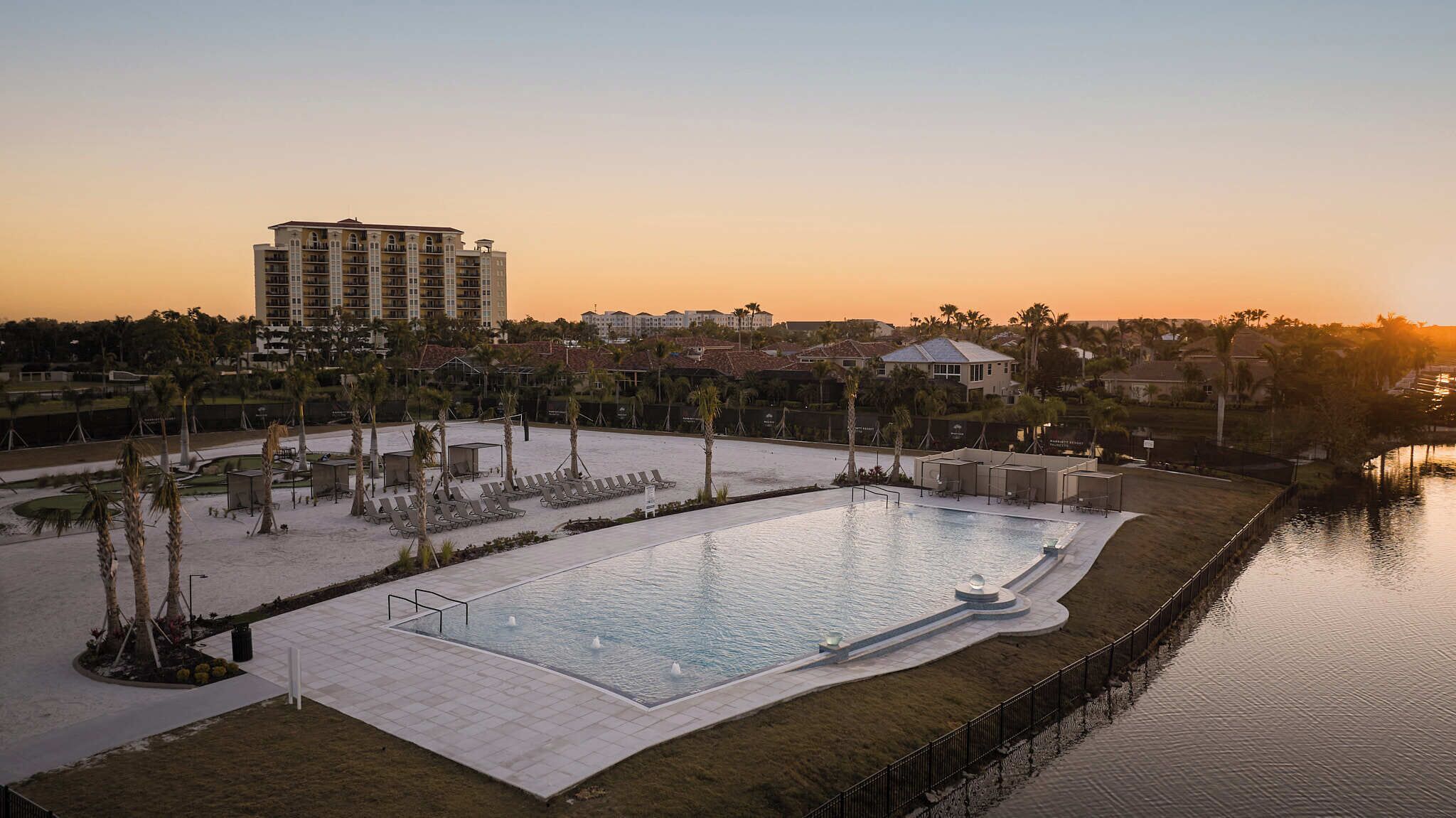 A large pool with lounge chairs and a water feature, surrounded by palm trees and a hotel building in the background.