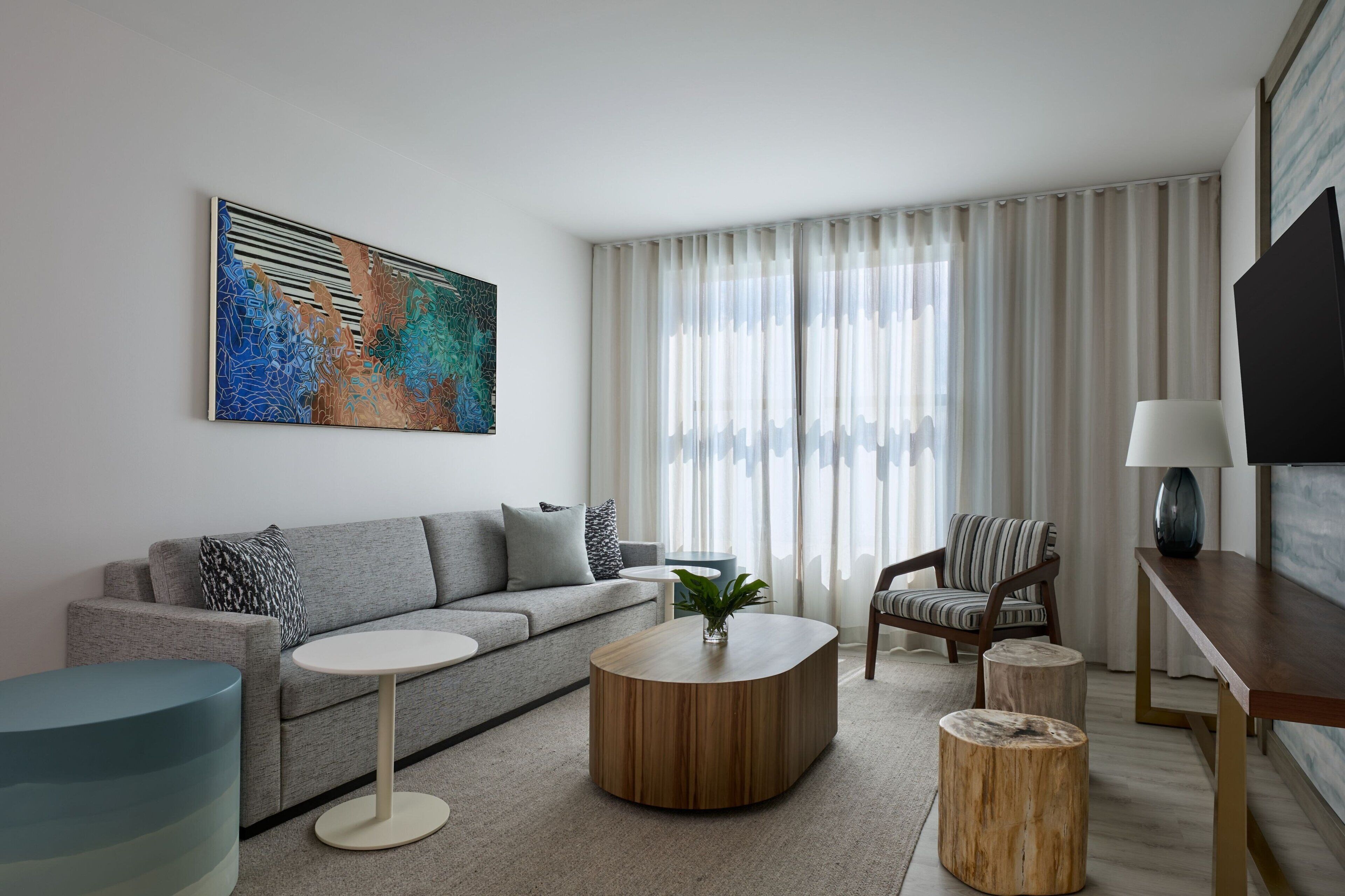 A modern living room with a grey sofa, a round coffee table, a striped armchair, and a TV on a wooden stand.