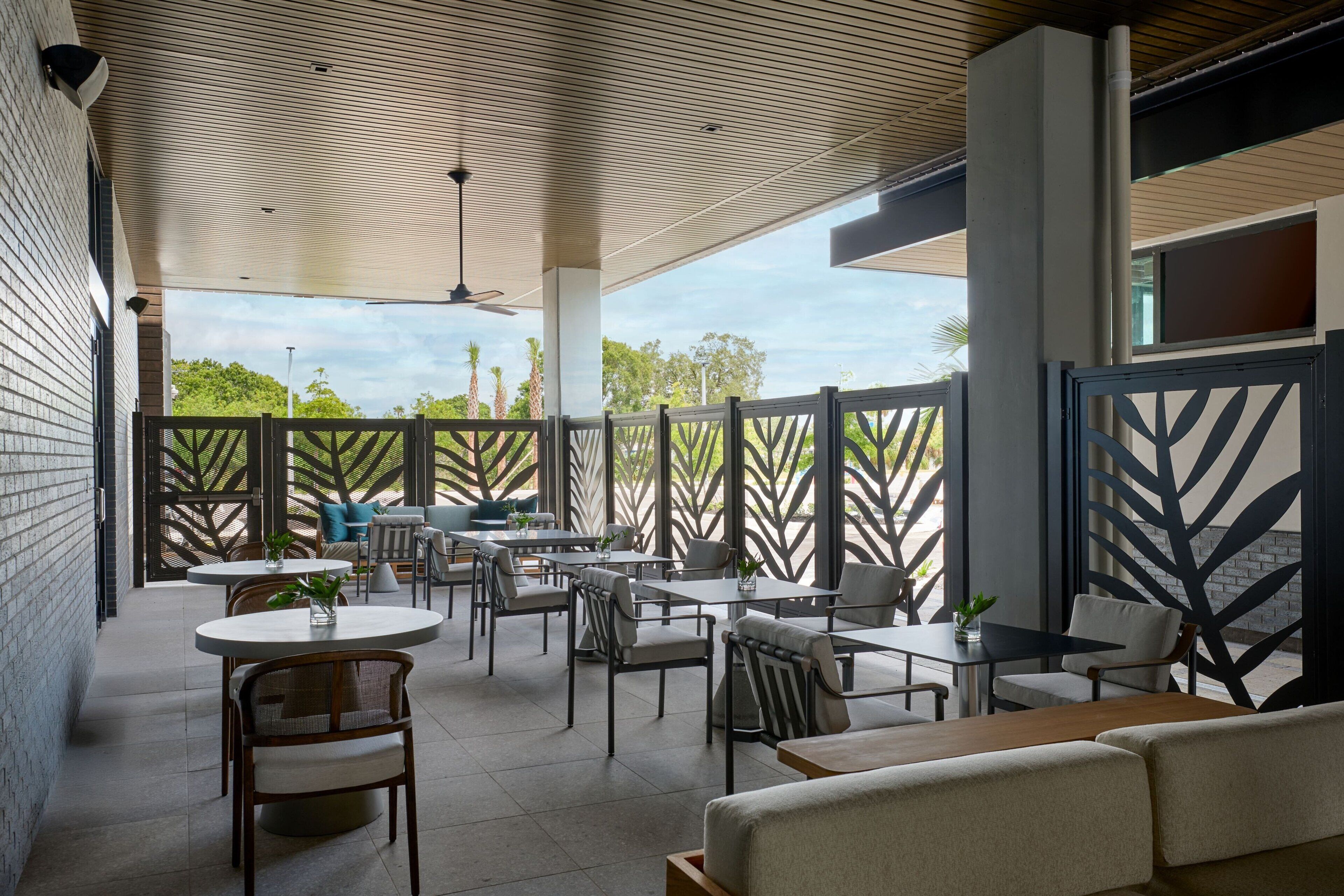 An outdoor patio with round tables and chairs, a sofa, and a view of palm trees.