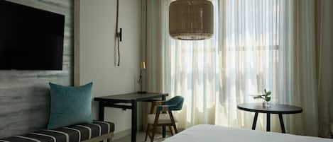 Habitación de hotel con cama, escritorio, sillón, sofá y televisor montado en la pared.