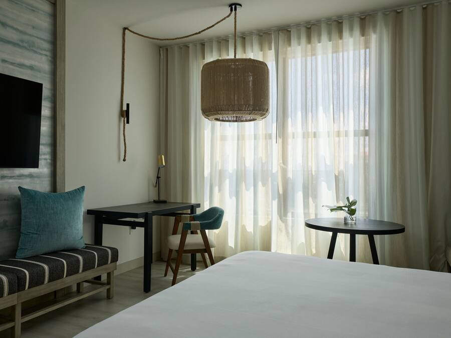 A hotel room with a bed, a desk, a chair, a sofa, and a TV mounted on the wall.
