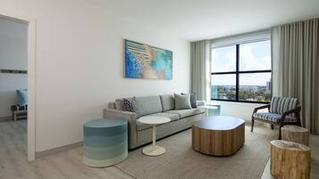 A modern living room with a grey sofa, a round coffee table, and a striped armchair. A large abstract painting is on the wall, and there is a window with curtains.