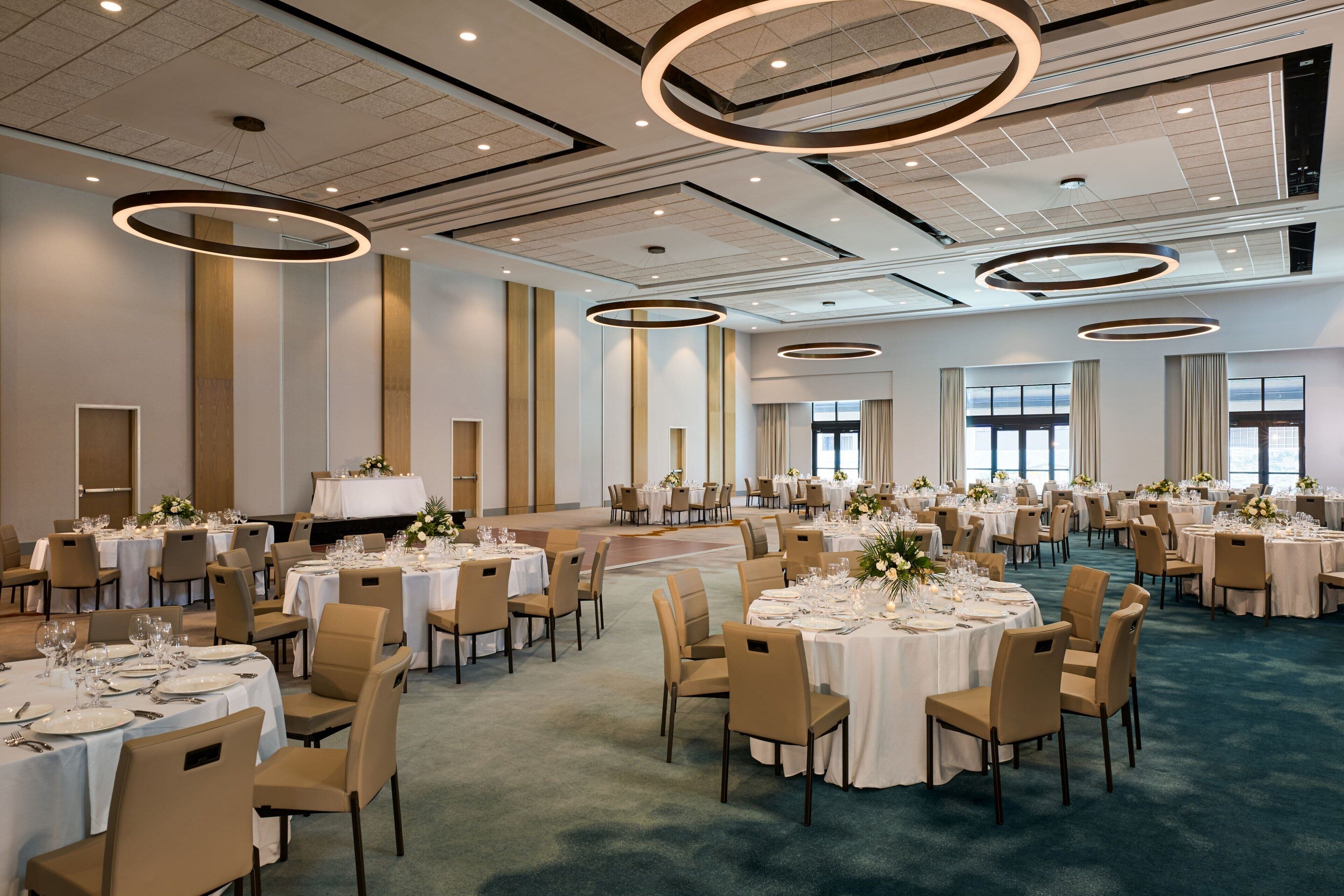 A spacious banquet hall with round tables, beige chairs, and a carpeted floor.